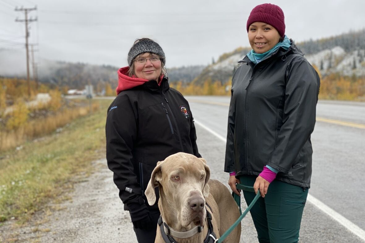 Two women standing with a dog on the side of the road