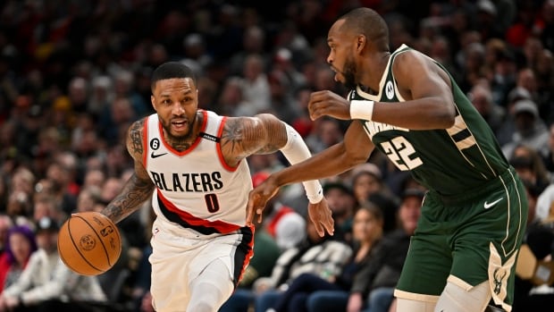 A basketball player dribbles the ball as an opponent defends.