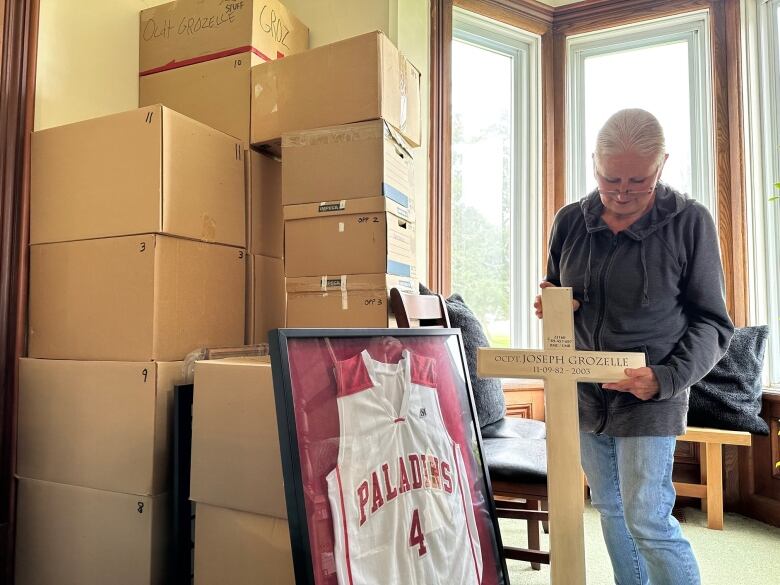 Joe Grozelle's mom looks down at the cross they were given from his military funeral in 2003. Minnie is standing beside boxes of Joe's belongings, some containing things like the clothes his body was found in three weeks after he disappeared.