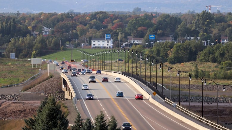 An overhead shot of a bridge with cars driving over it, with forest on the horizon.