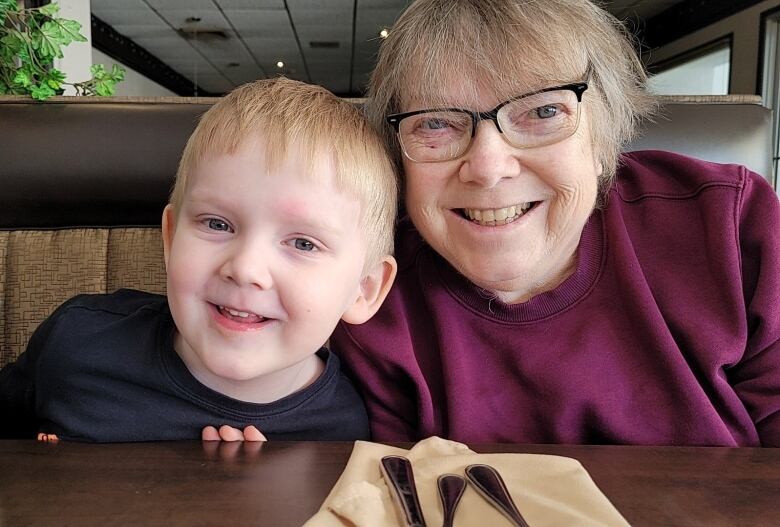 A close of portrait of a young boy and an older woman, both smiling, who are sitting at a table.