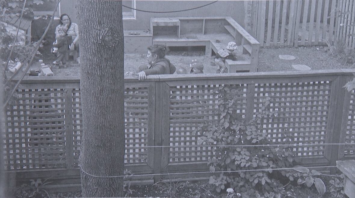A black and white photo of children and educators in a yard. 