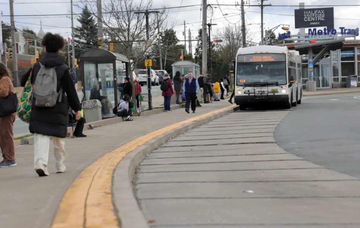 A shot shows the main loading area at Mumford Terminal. In the background passengers board a bus in front of the main terminal building.