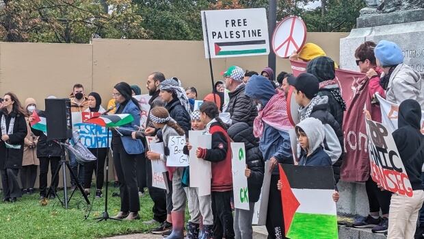 Rania Farouk Ismail speaks to people who showed up to the vigil Saturday. She said she knows many people with families in Palestine who are scared. A woman speaking to a microphone, surrounded by people carrying signs and Palestinian flags.