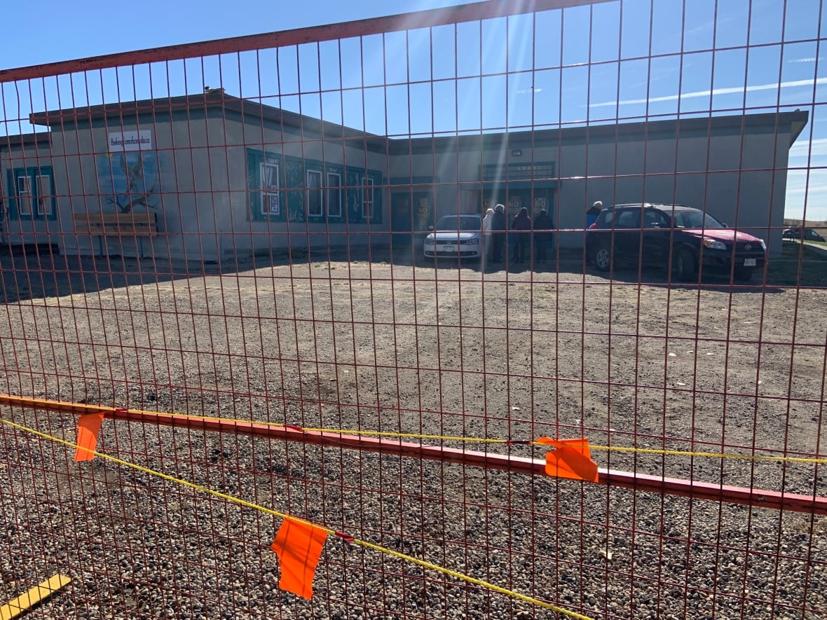 There is a red fence around a school and several people are gathered near the building