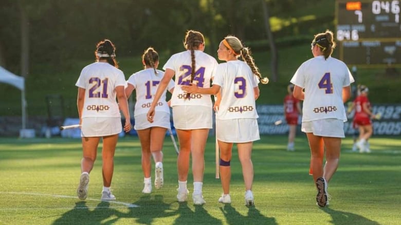 Female lax players pat each other on the back, on the field in the sunset.