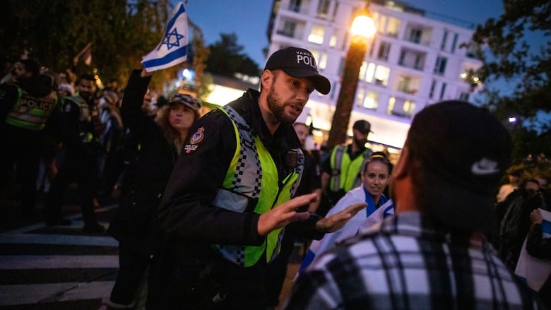 A police officer speaks to a protester with some people holding Israeli flags behind him.