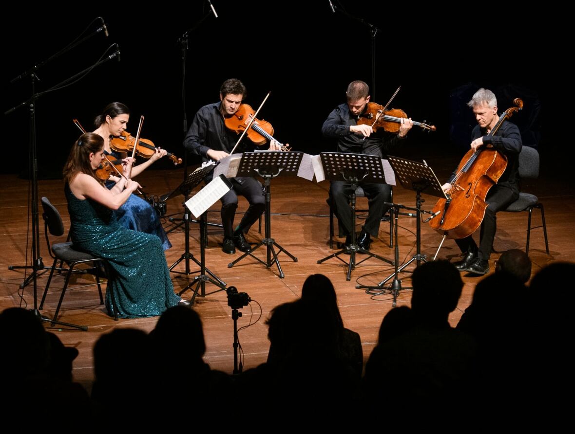 Five classical musicians, two women and three men, perform on the stage of a concert hall