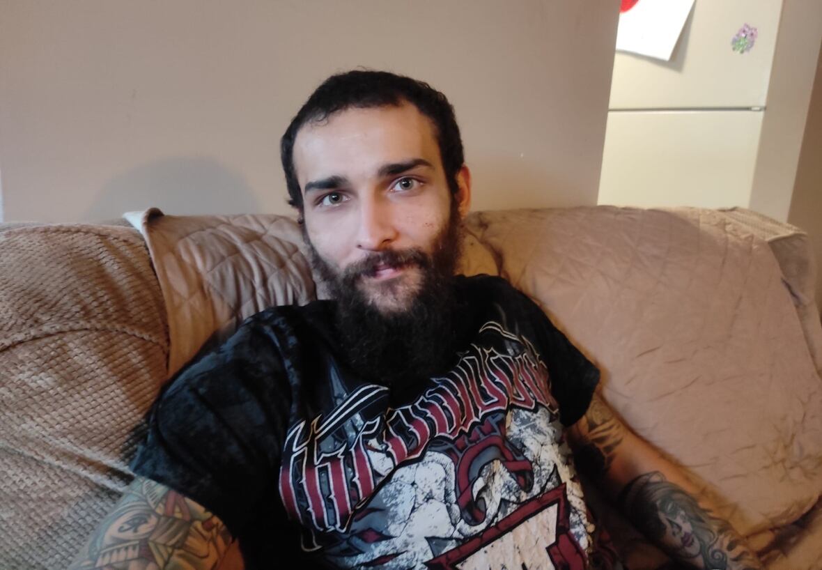 Man with a black shirt and a beard sits on a sofa