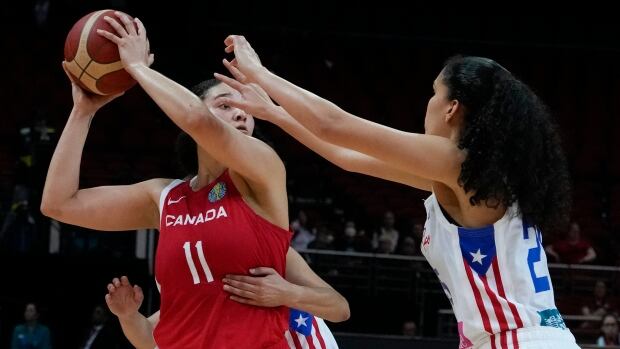 A women's basketball player looks to pass the ball past her opponent.