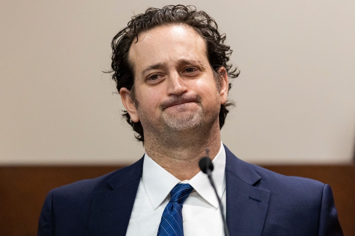A man in a suit and tie speaks from a court witness stand.