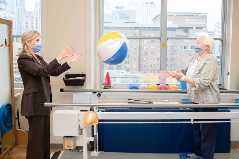 A person throws a large ball to another person in a hospital therapy room.