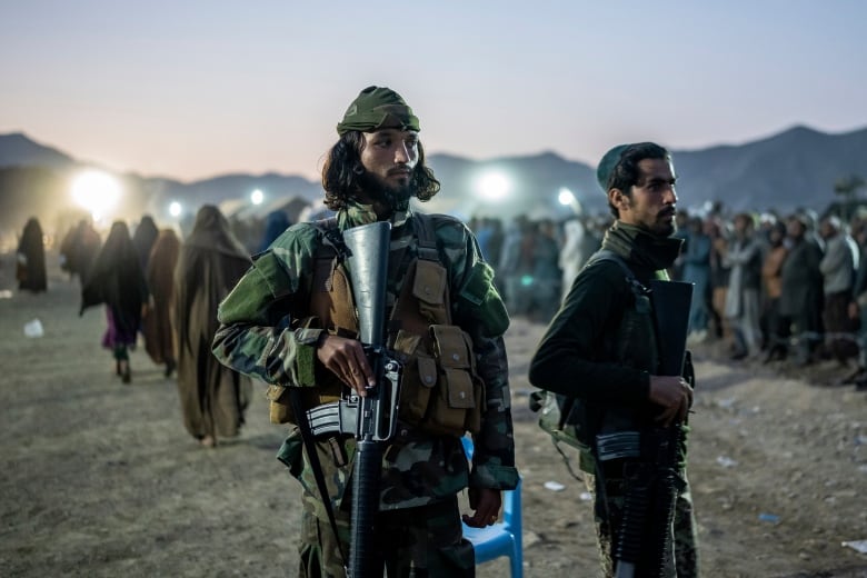 Armed men in fatigues walk through a refugee camp.