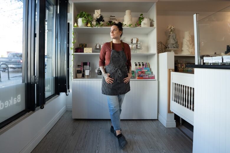 A white woman wearing a denim apron poses in front of a bakery display.