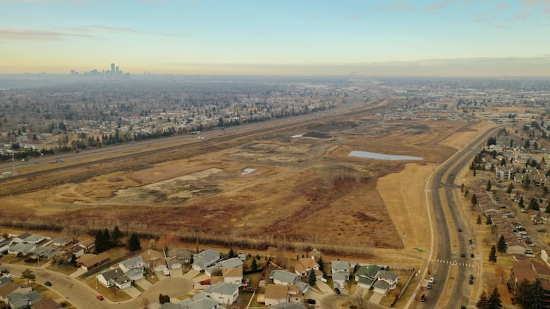 An aerial view of a large empty lot. A row of houses can be seen in the foreground.