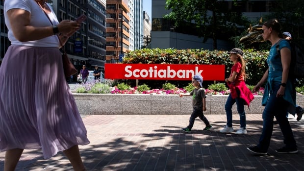 Pedestrians walk past a Scotiabank sign.