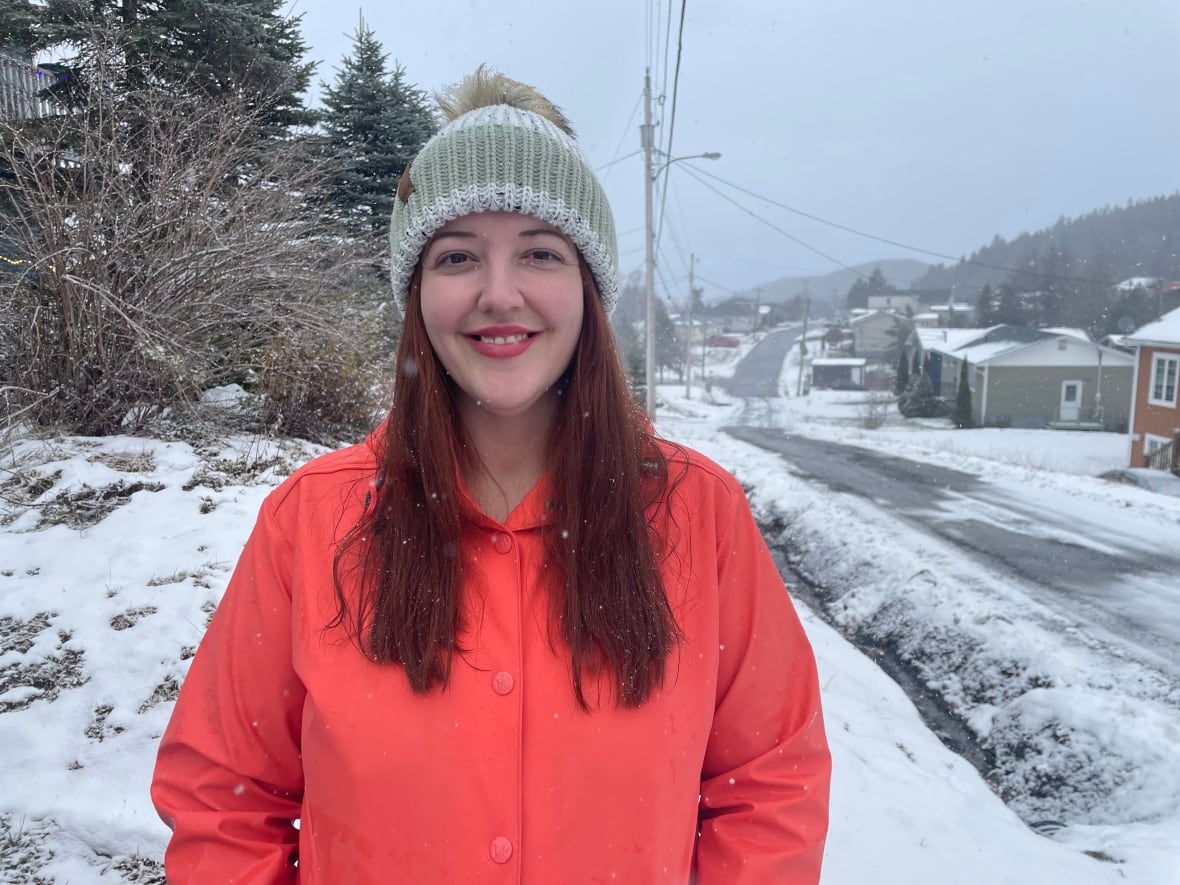A woman with long red hair wearing a red coat stands at a snowy intersection.