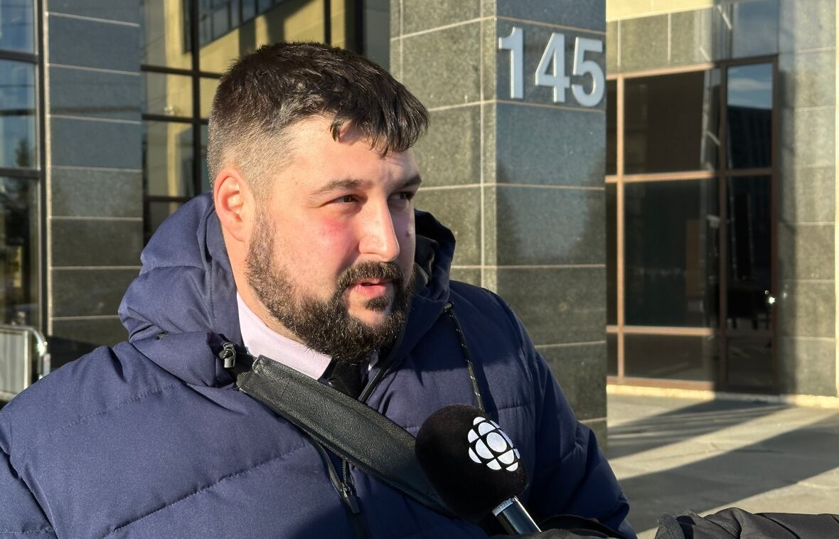 A man in a blue winter coat speaking into a CBC-branded microphone. 