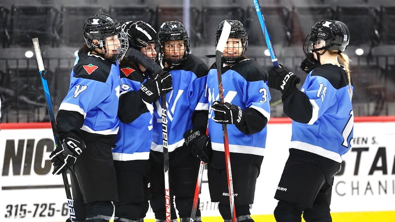 A group of female hockey players in bright blue jerseys celebrate on the ice.