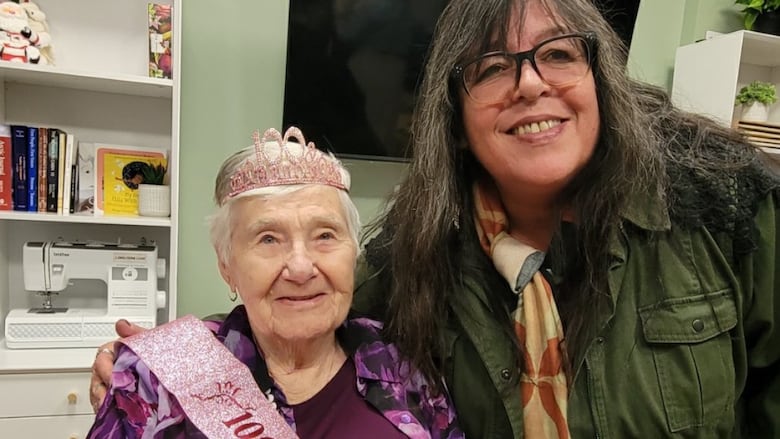 An old woman in a purple sweater wears a sash that reads "100 and fabulous"