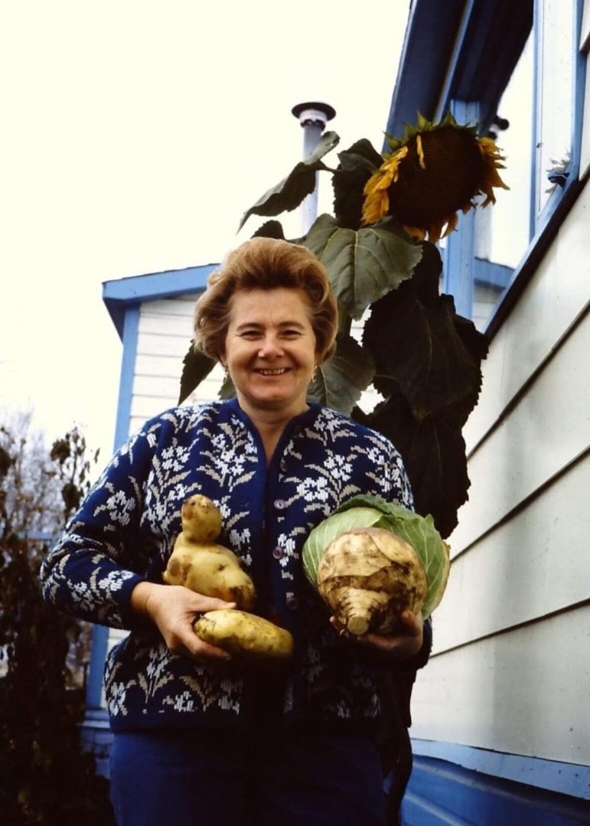 A woman holds vegetables from her garden, including a potato and a cabbage.