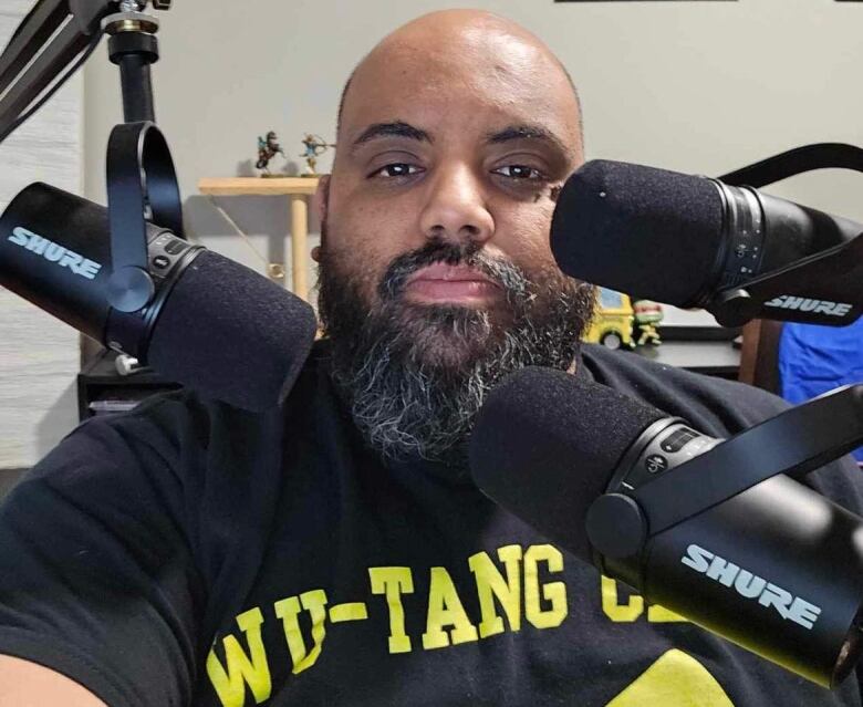 A black man sits behind two microphones.