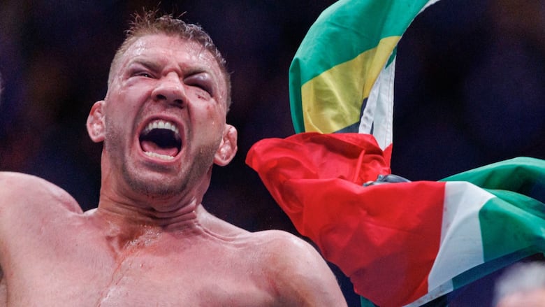 A sweaty UFC fighter with a black eye celebrates his win by waving his country's South African flag.