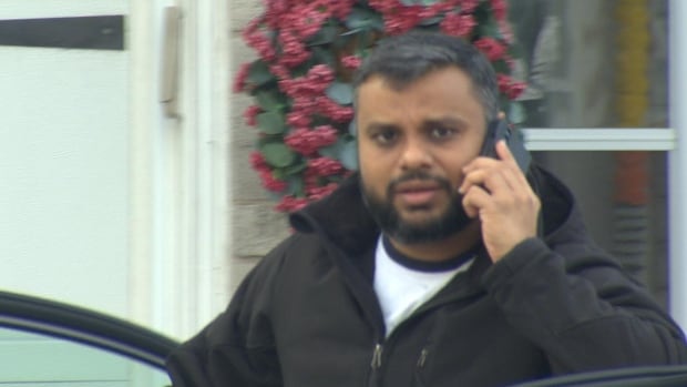 A man holds a cellphone as he gets out of a car on his driveway, not realizing his photo is being taken 