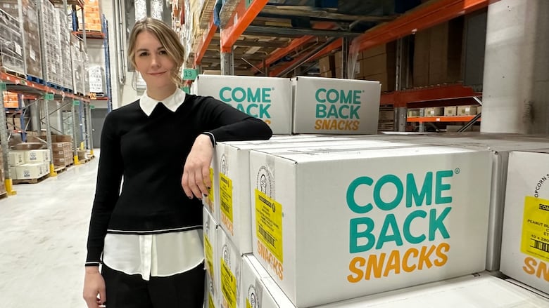 Photo of Emily O'Brien in a distribution warehouse, leaning against boxes labelled 'Comeback Snacks.'