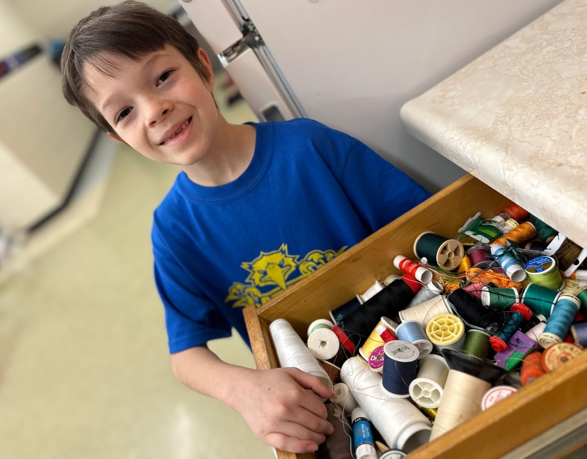 A boy stands in front of a drawer filled with thread. 