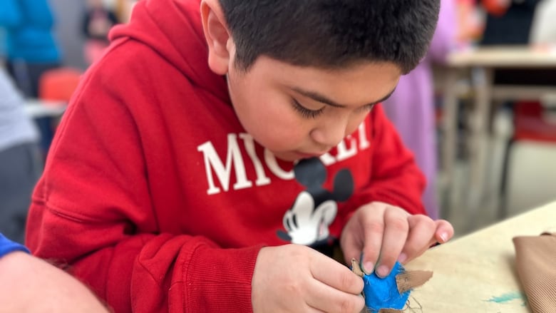 A little boy sews. 