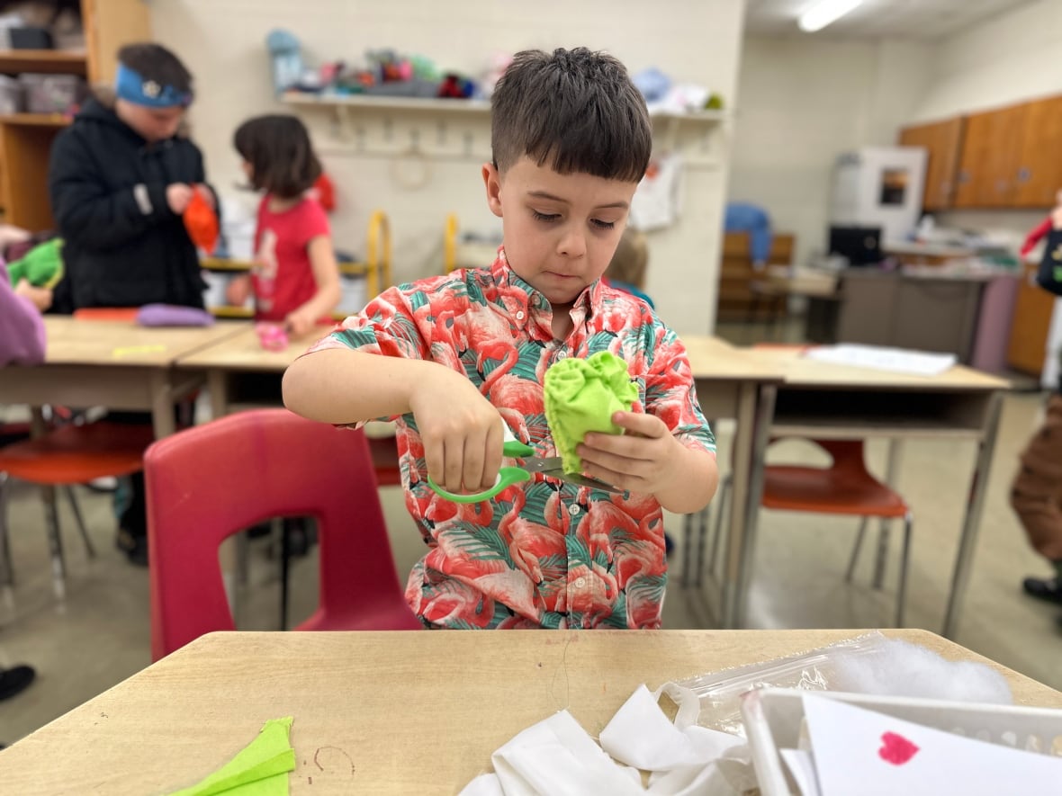 A boy holds up green fabric and scissors. 