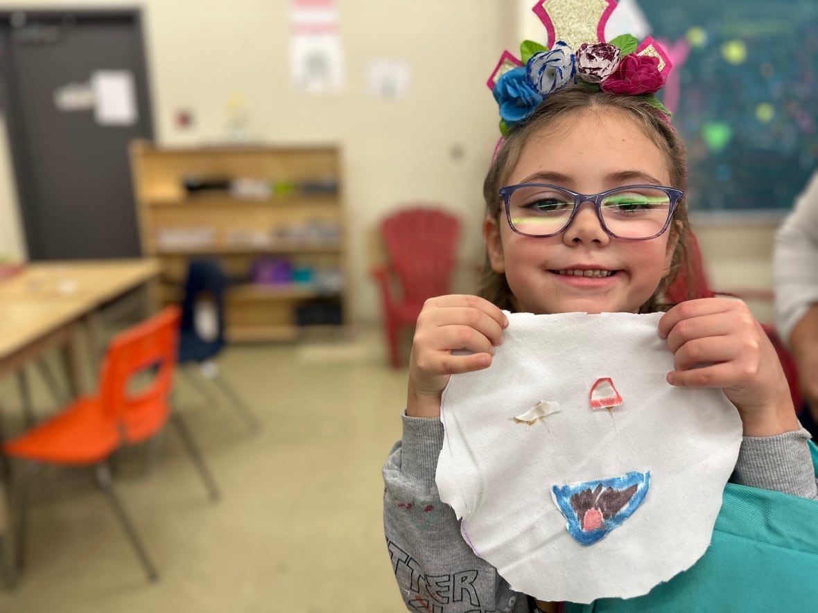A girl holds up a thing she sewed. 