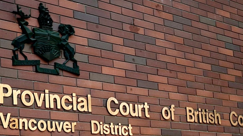 A sign on a brick walls says "Provincial Court of British Columbia Vancouver District" with a crest.
