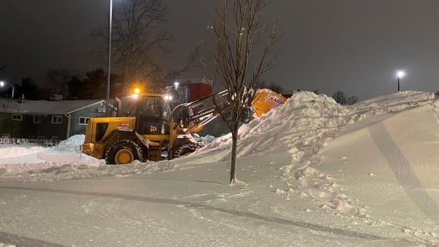 A snow plow at work in a parking lot at night.