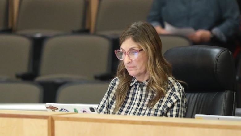 A woman in a black and white check shirt sits at a desk. 