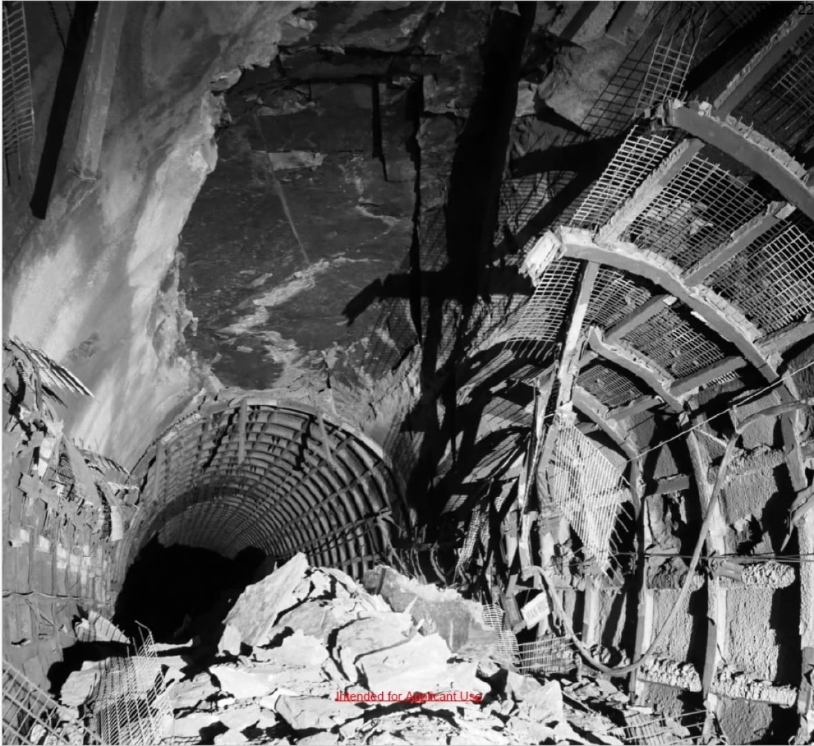 A black-and-white image of a pile of rocks in the middle of a dark tunnel, lit up by the flash of a camera, with bent steel hanging from the roof.