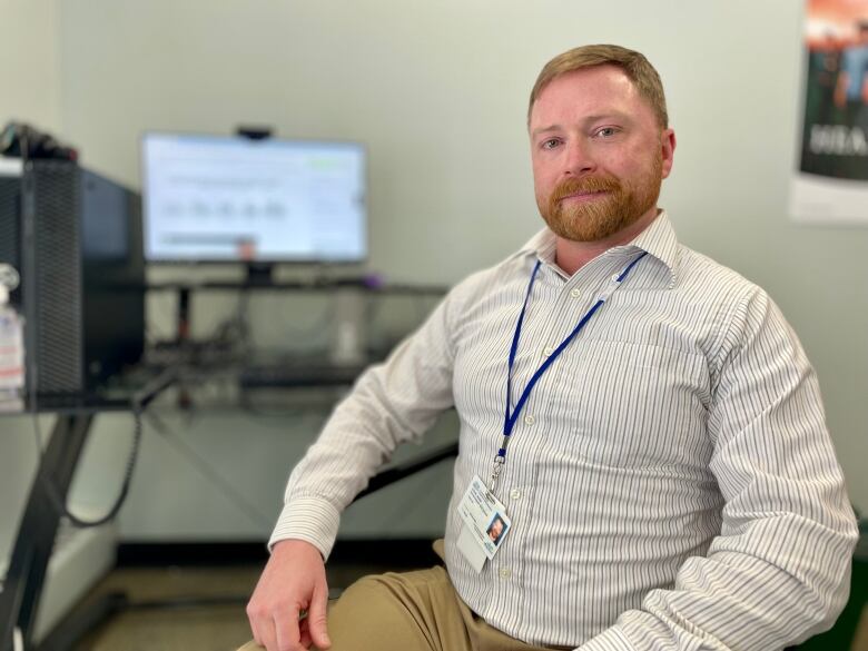 Colin Hood sits in a chair with a computer positioned over his shoulder.