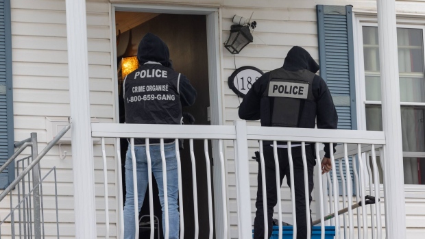 Quebec police make more arrests in organized crime sweep; Police officers on the front porch of a house facing an open door\. 