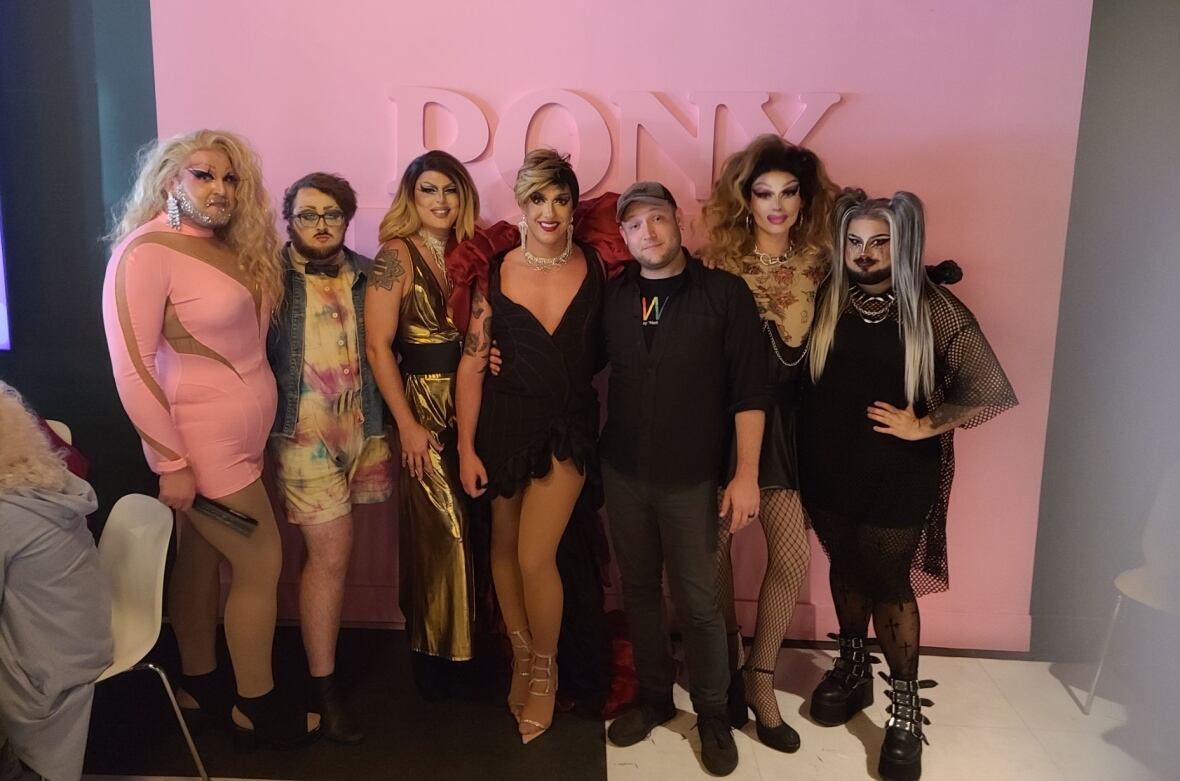 A group of drag artists pose with man. 