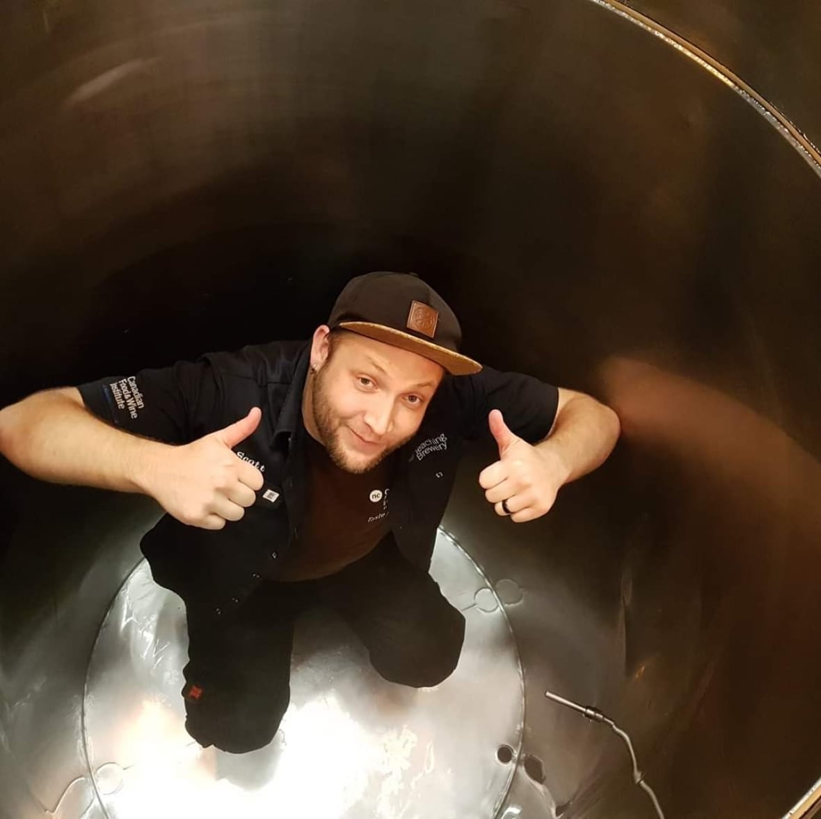 A man smiles and gives two thumbs up from inside a beer brewery barrel