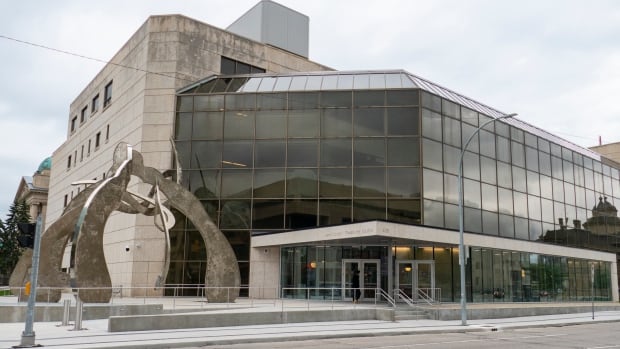 A glass-fronted building features a large piece of public artwork outside the front doors.
