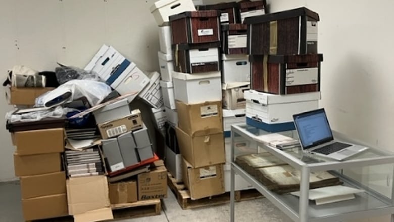 a bunch of old boxes, pictures and plaques sit in a disheveled pile in a basement room. 