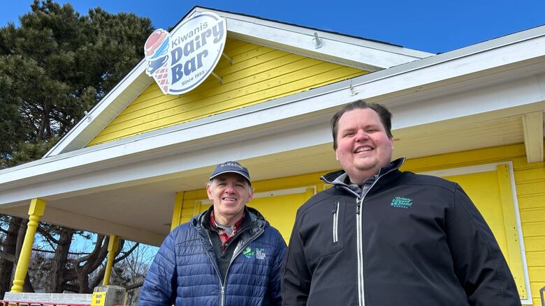 Two men stand infront of a closed ice cream shop.