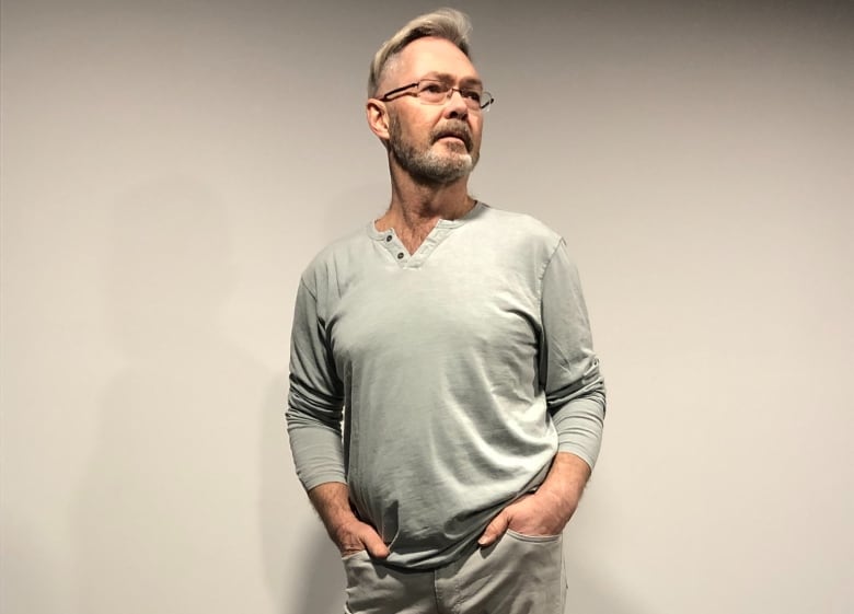 A man in a grey shirt and glasses looks off to the right.