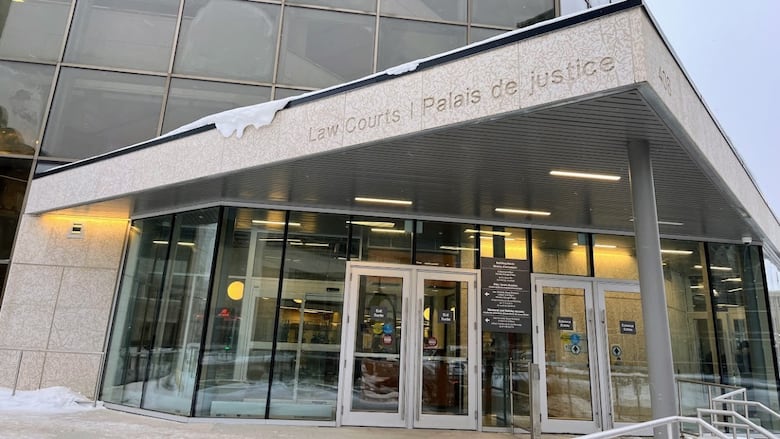 A glass and stone building is seen from outside. A name carved above the doors says Law Courts.