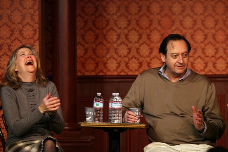 A woman laughs next to a man who is in the middle of speaking.