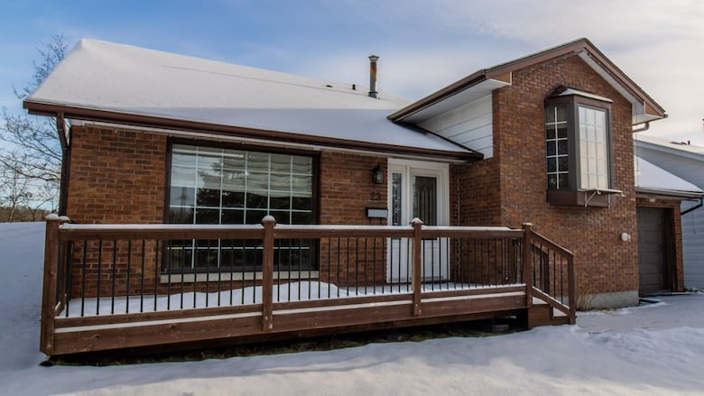 A small brick house is seen during the day time, with snow on the roof and in the front yard.