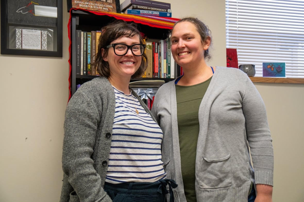 Two people stand in front of a bookcase, smiling.
