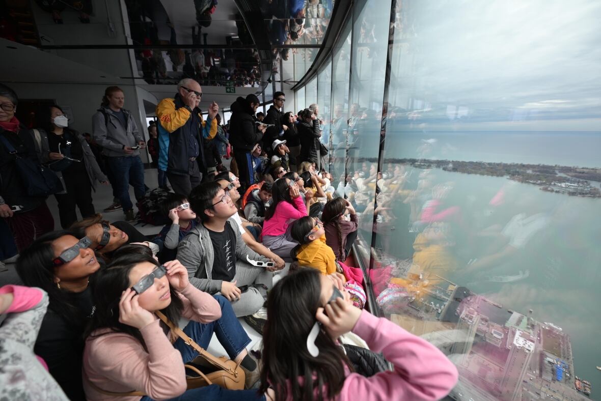 Image inside the CN tower showing visitors peering outside the window wearing their glasses. 